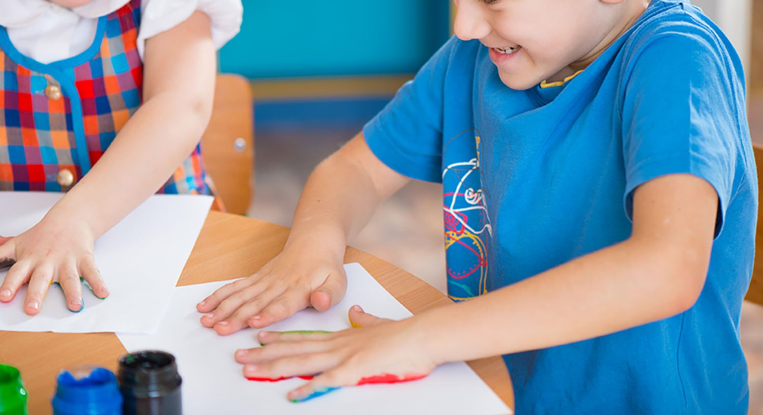 Cute preschool children painting with their palms at kindergarten being creative for their school tea towel fundraiser