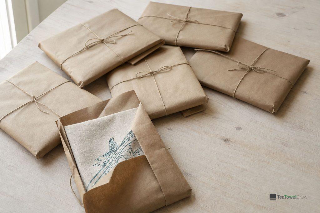 Commemorative tea towels wrapped in kraft paper parcels, one partly opened to show the printed cloth.