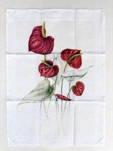 A tea towel printed in full colour with a botanical painting of red anthurium flowers.