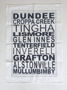 A white tea towel printed with northern NSW town names in bold black type, including Dundee, Glen Innes, Grafton and Mullumbimby.